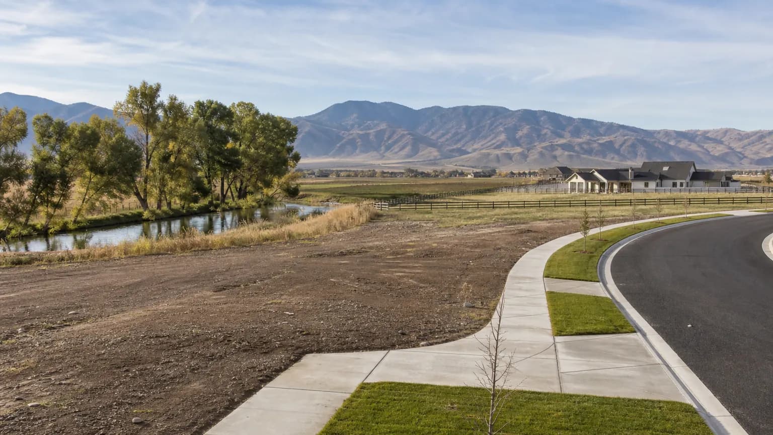 Edge of Treasure Valley farmland with a new subdivision, concrete sidewalks and curbs, and an irrigation canal lined with cottonwoods